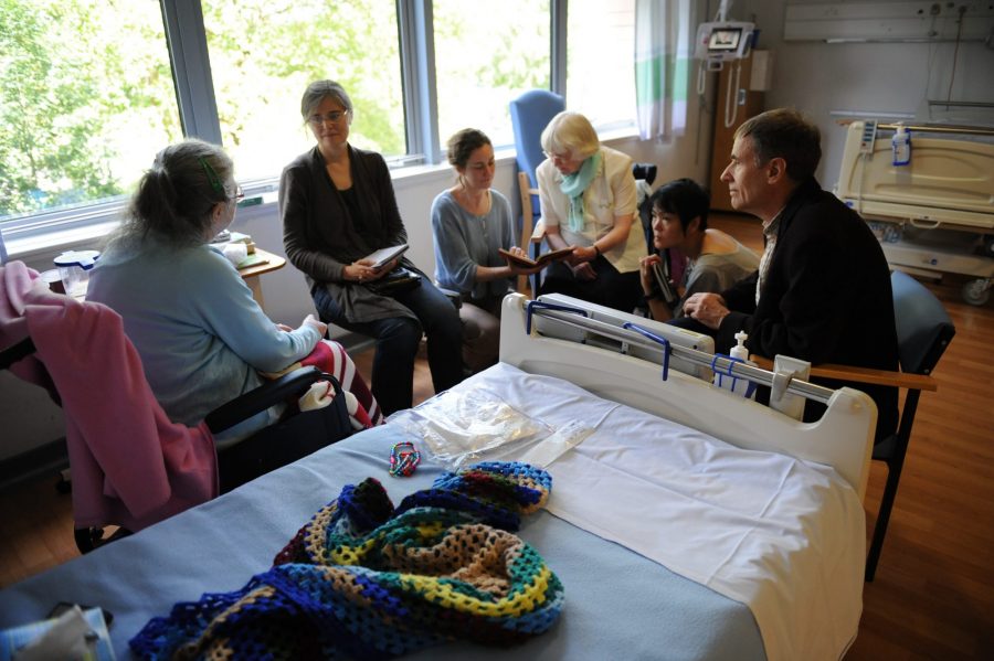 Artists and volunteers collaborate with artist patients around a hospital bed