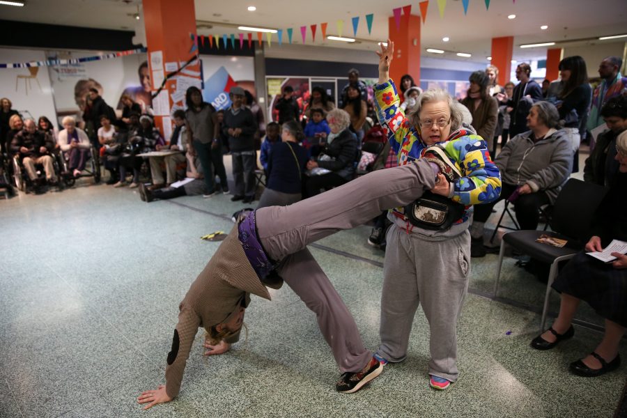 man doing handstand older woman holding leg up