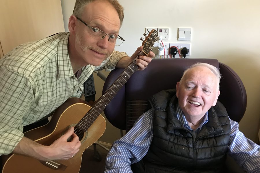 man playing guitar and older man in chair