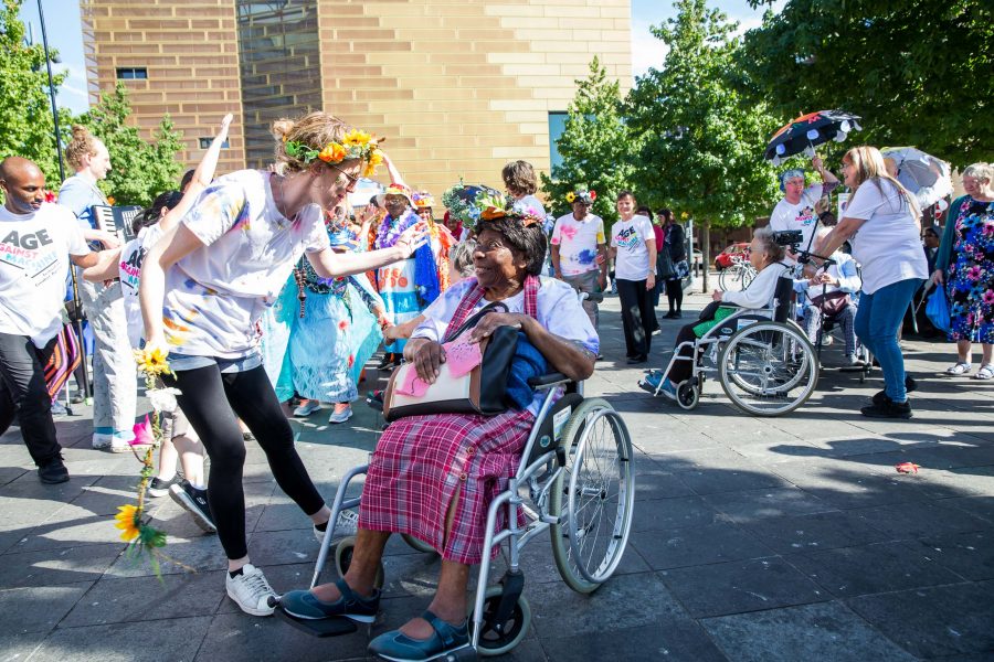 woman in wheelchair smiling and arm waving with a group of people