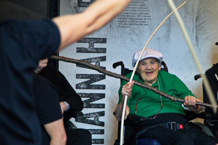 Two elderly men in wheelchairs wearing green shirts and smiling.