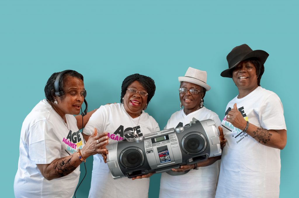4 people smiling holding an old style ghetto blaster