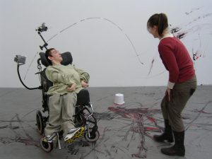 Girl in wheelchair and artist splashing paint around a room