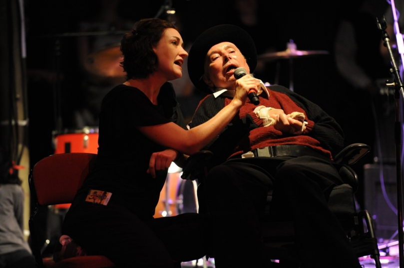 man in wheelchair singing into microphone held by a women