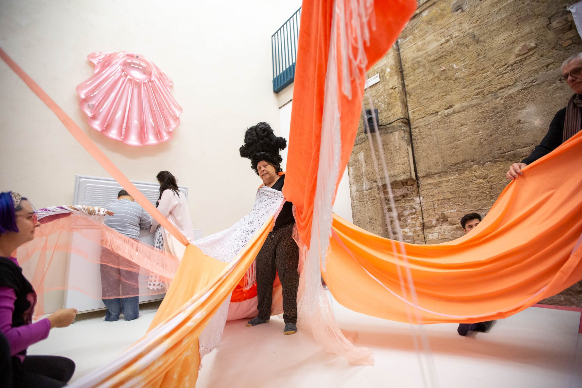 man dressed in large curly black wig with fabrics draped from the ceiling