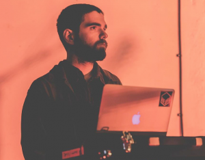 Man with short dark hair and beard making music on a computer