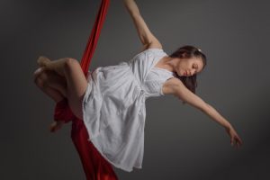 Woman suspended on a red cloth acobatically poised