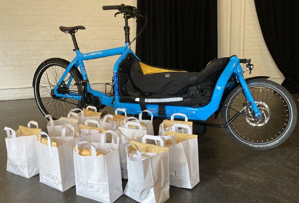 A blue bicycle that can carry cargo with packages in neat rows next to it.