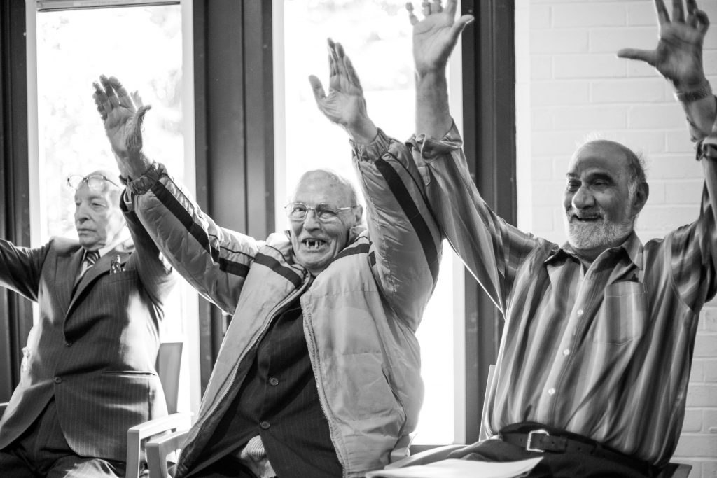 three older men smiling with their arms raised in the air.