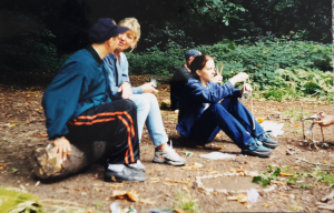 four people sitting ina wood on a log talking