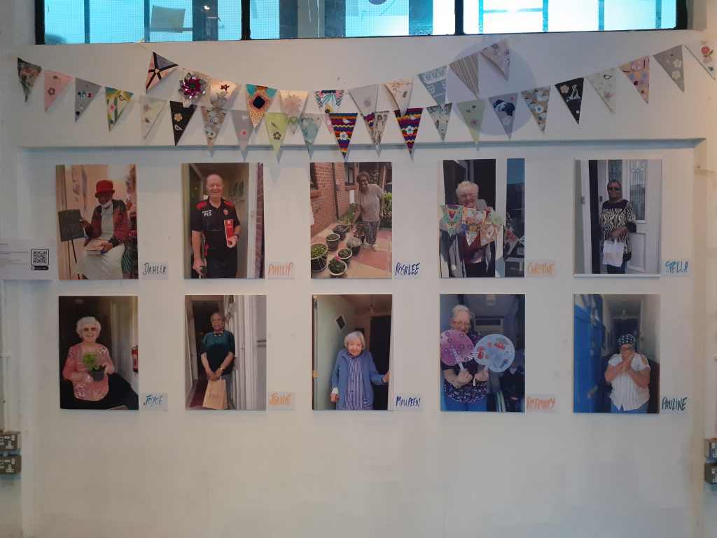 A white wall with photos of older people and colourful bunting hanging at the top